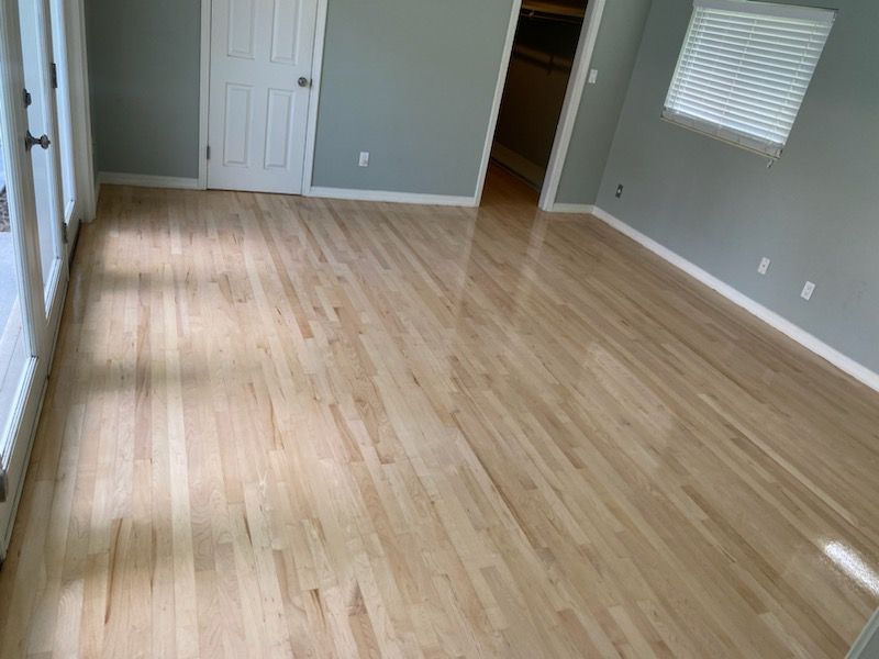 Empty room with light wood floors, gray walls, white trim, and a window with blinds.