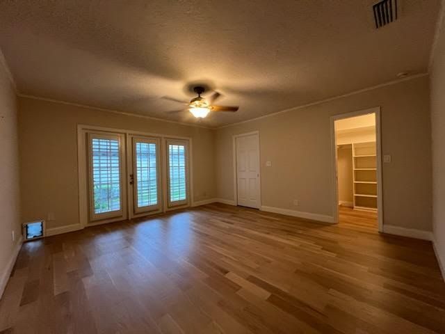 Empty living room with hardwood floors, ceiling fan, French doors, and open doorway to a closet.