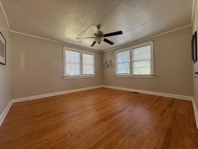 Empty beige room with hardwood floor, two windows, and a ceiling fan.