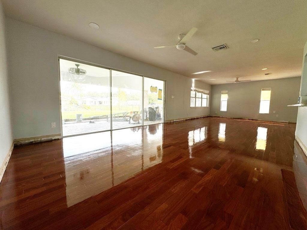 Empty living room with polished wood floors and large sliding glass doors to a bright patio