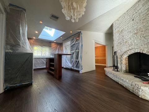 Living room under renovation with covered furniture, dark floors, skylight, and stone fireplace