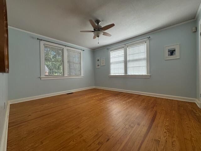 Empty room with hardwood floor, light blue walls, ceiling fan, and two windows with white blinds