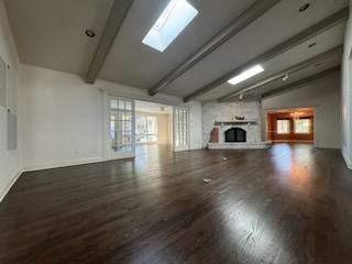Empty modern living room with dark wood floors, white walls, fireplace, and skylights