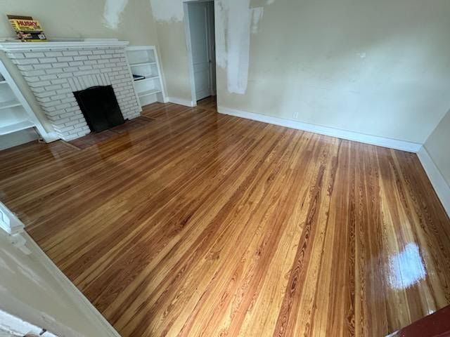 Empty room with polished hardwood floor, white walls, and a white brick fireplace.