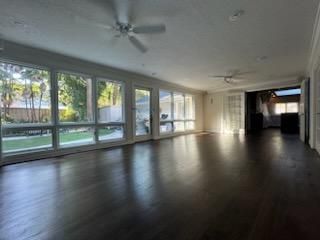 Empty modern living room with large windows, dark floors, and ceiling fans, lit by daylight