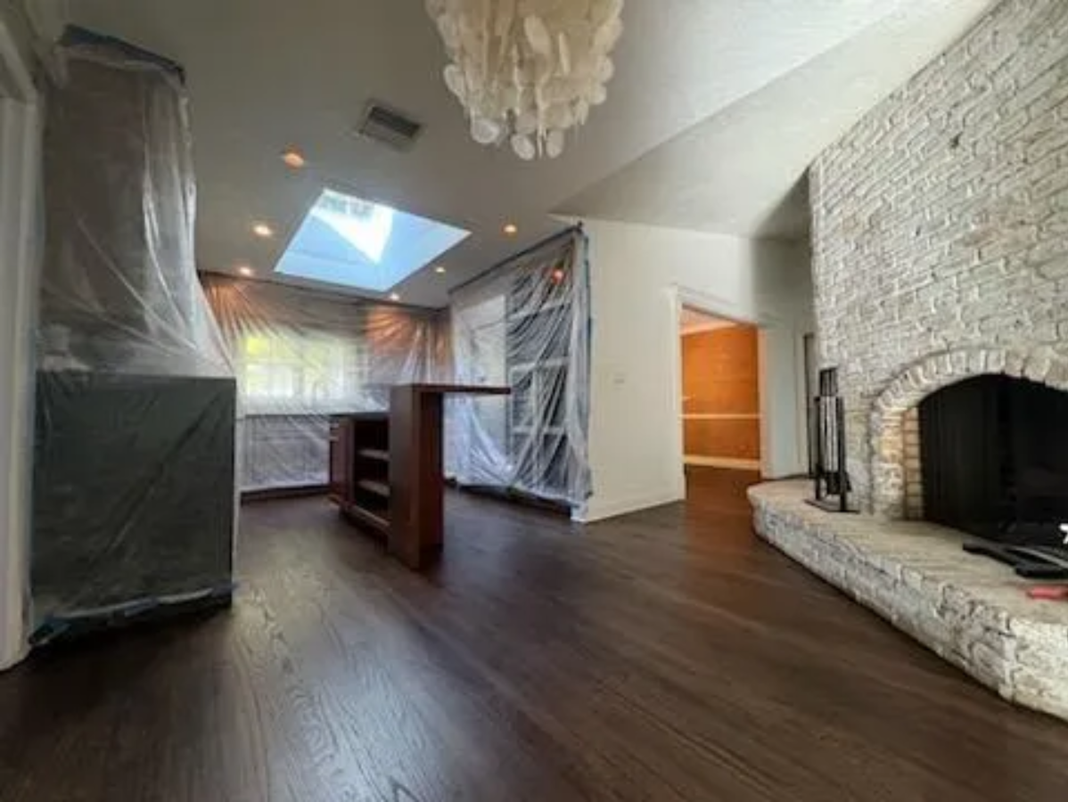 Spacious room with dark wood floors, stone fireplace, skylights, and wrapped cabinets under renovation