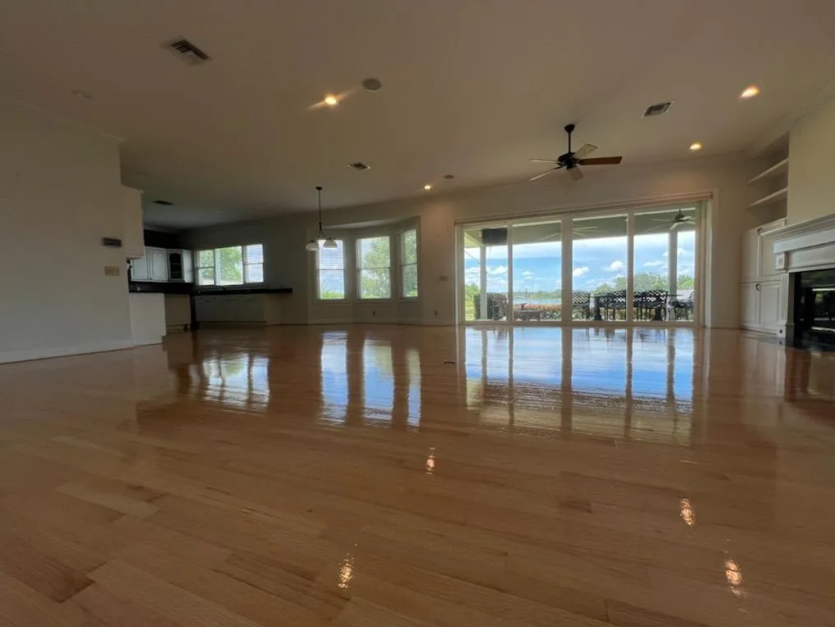 Spacious empty living room with polished wood floors, recessed lights, and large glass doors to a patio and ocean view