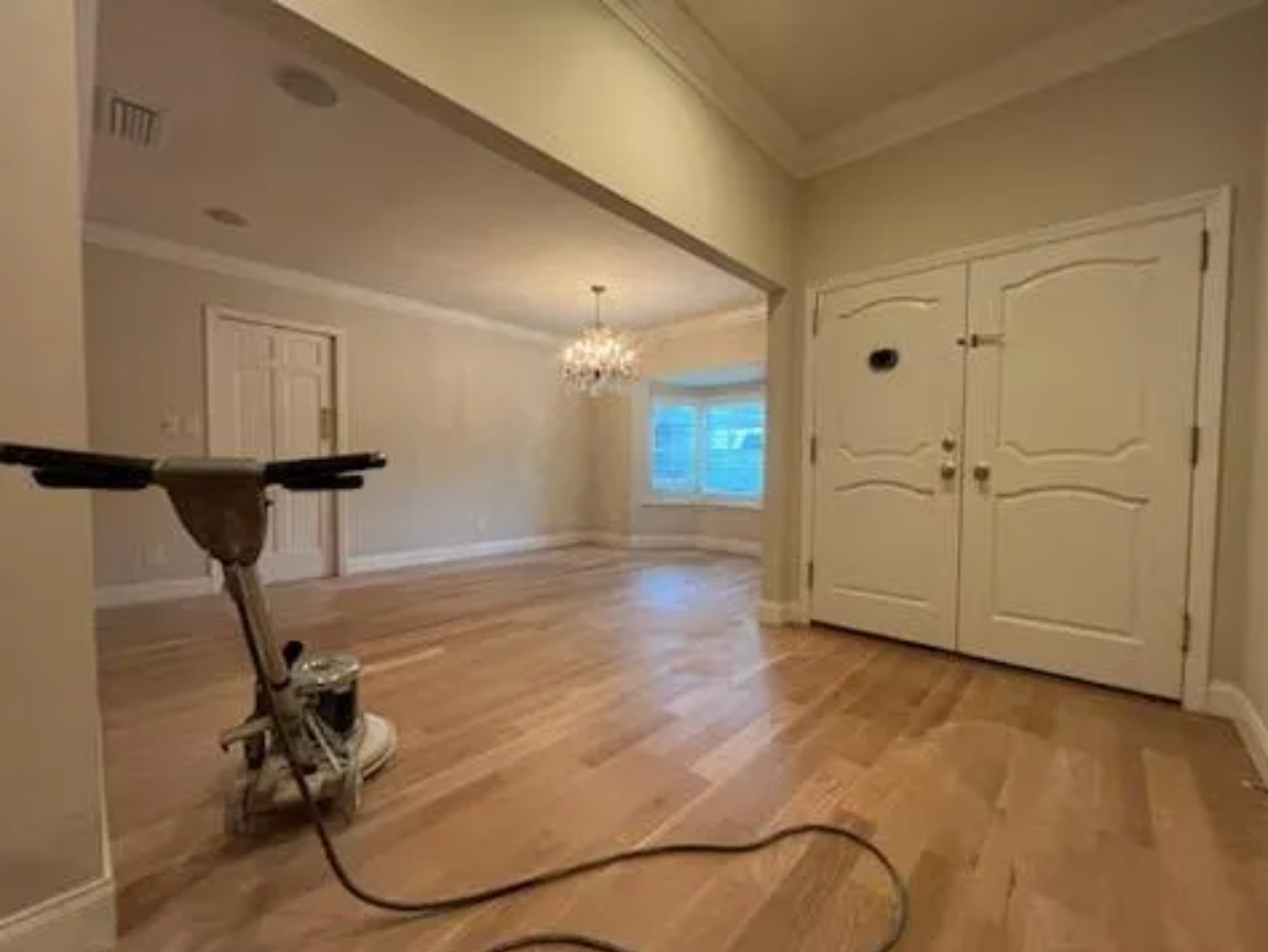 Empty room with hardwood floors, chandelier, and a vacuum cleaner in the foreground