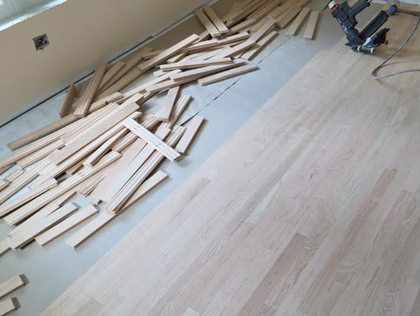 Wood flooring installation with scattered planks and a nail gun in a room under construction