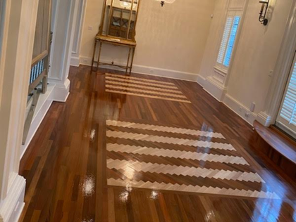 Shiny hardwood hallway with a striped rug and sunlight casting shadows through windows