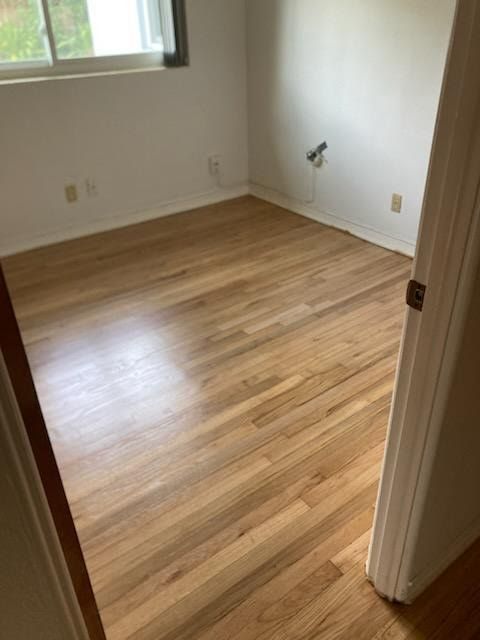 Empty room with hardwood floors, white walls, and a window letting in daylight.