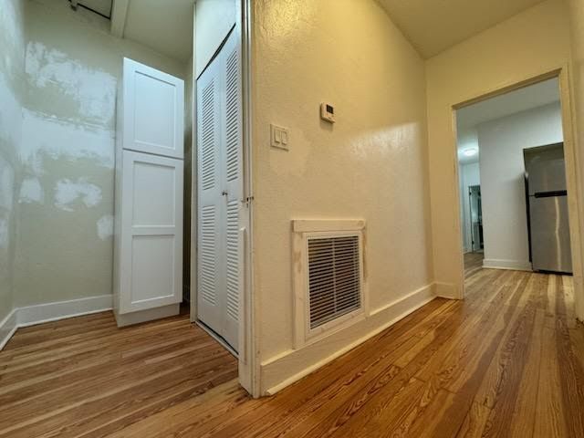 Empty hallway with hardwood floors, white walls, closet doors, and a vented panel near a doorway