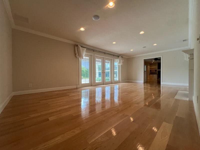 Empty living room with glossy hardwood floors, recessed lights, and French doors opening to a green view