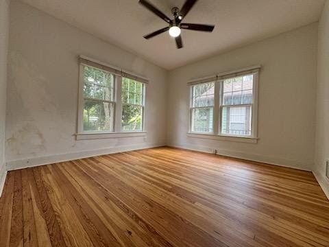 Empty room with hardwood floors, white walls, ceiling fan, and two windows with blinds