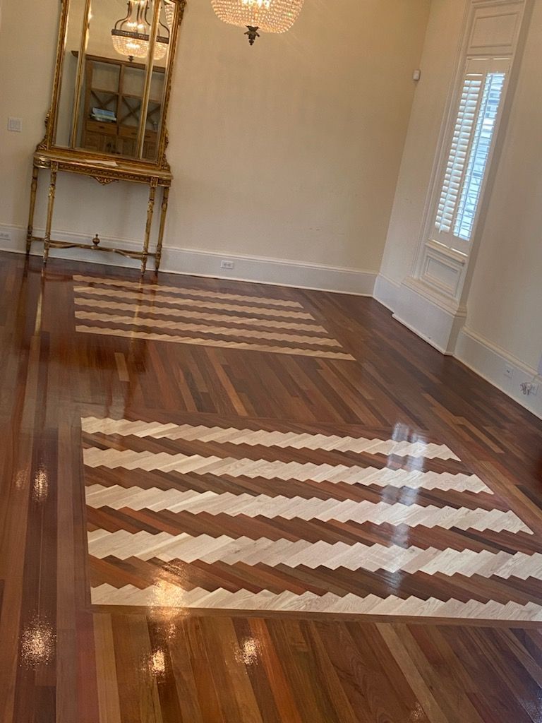 Empty room with hardwood floor, striped rug, mirrored console, and window blinds casting light on the wall.