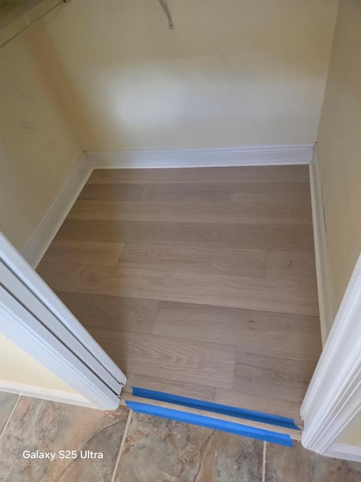 Empty closet with light wood floor and blue tape marking the threshold