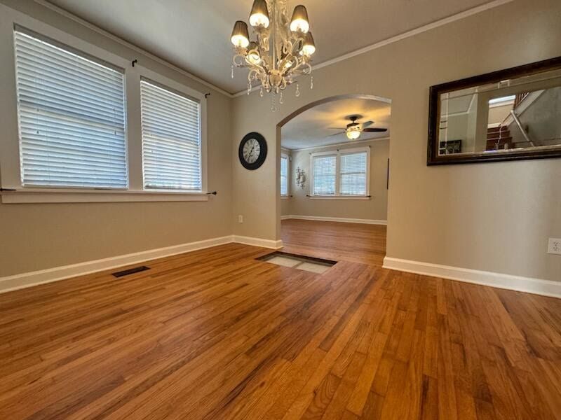 Empty dining room with hardwood floors, chandelier, windows, and arched doorway to a bright adjoining room