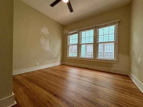 Empty beige bedroom with hardwood floors, large window, and a ceiling fan