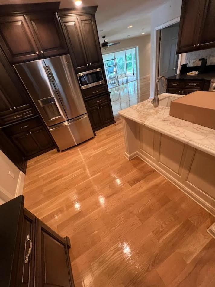 Modern kitchen with dark wood cabinets, stainless steel fridge, marble island, and a cardboard box on the counter.