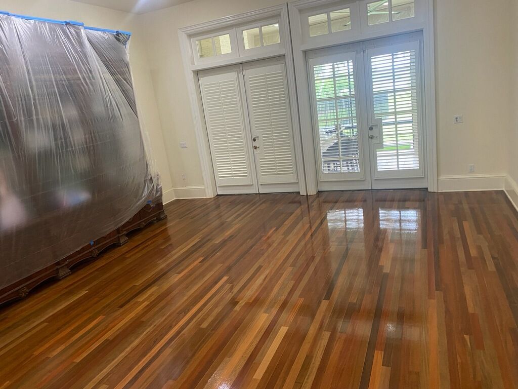Empty room with polished hardwood floors, white shutters, and a covered sofa on the left.