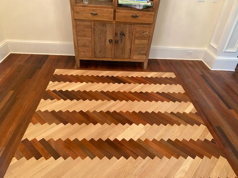 Wooden geometric-pattern rug on a hardwood floor in front of a small wooden cabinet