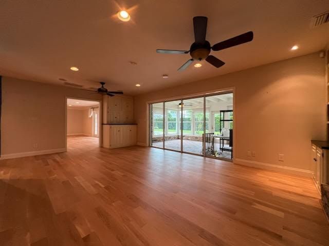 Empty open-plan living room with hardwood floors, ceiling fans, and sliding glass doors to a patio.