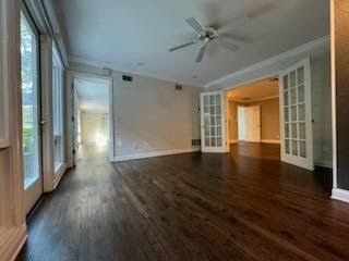 Empty living room with dark wood floors, white walls, ceiling fan, and French doors to a lit adjoining room