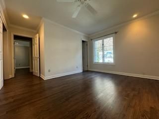 Empty living room with dark wood floors, beige walls, and a window letting in daylight