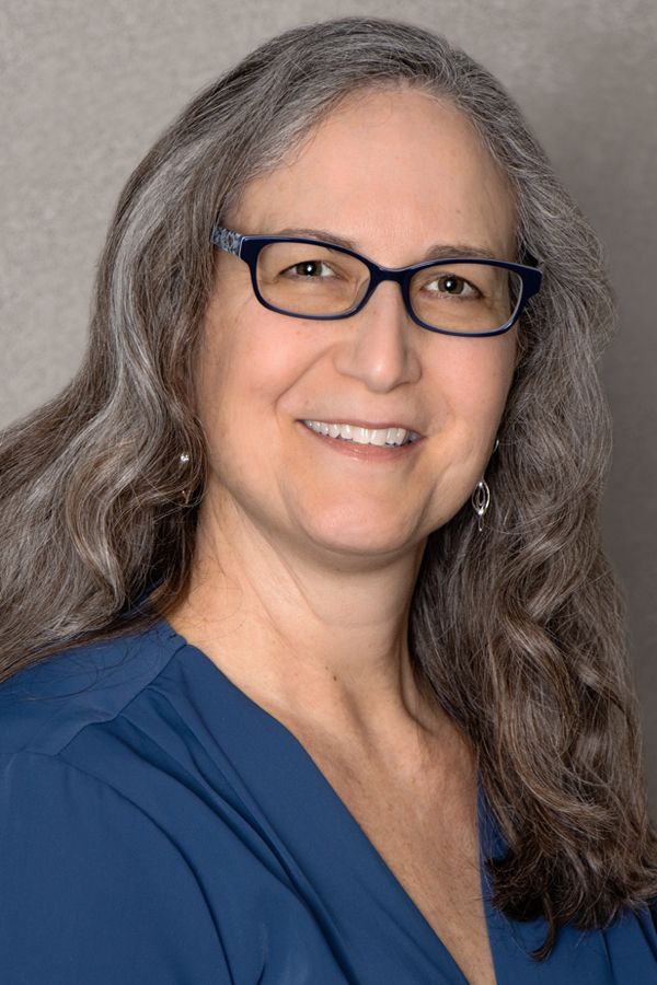 A woman wearing glasses and a blue shirt is smiling for the camera.