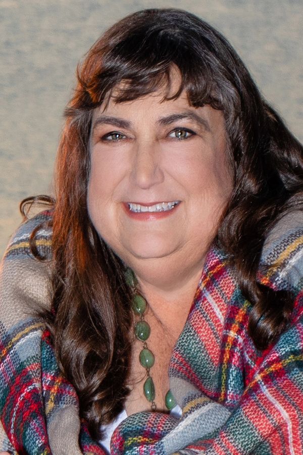 A woman wearing a plaid shirt and a necklace is smiling for the camera.