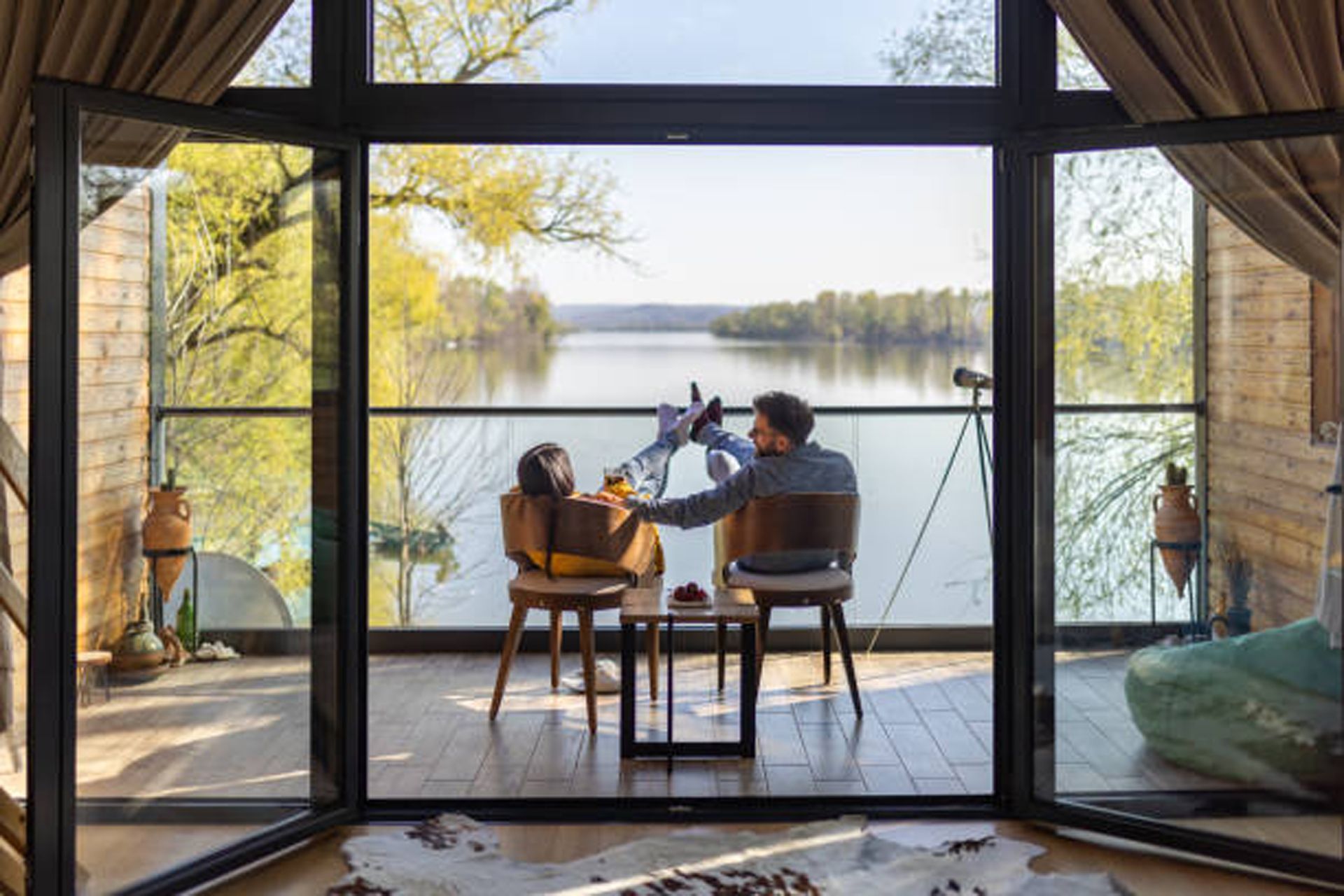 A man and a woman are sitting at a table on a balcony overlooking a lake.