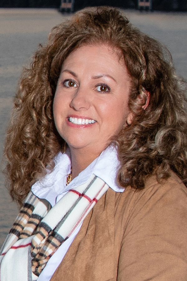 A woman with curly hair and a scarf around her neck is smiling for the camera.