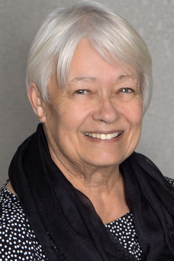 A woman with white hair and a black scarf is smiling for the camera.