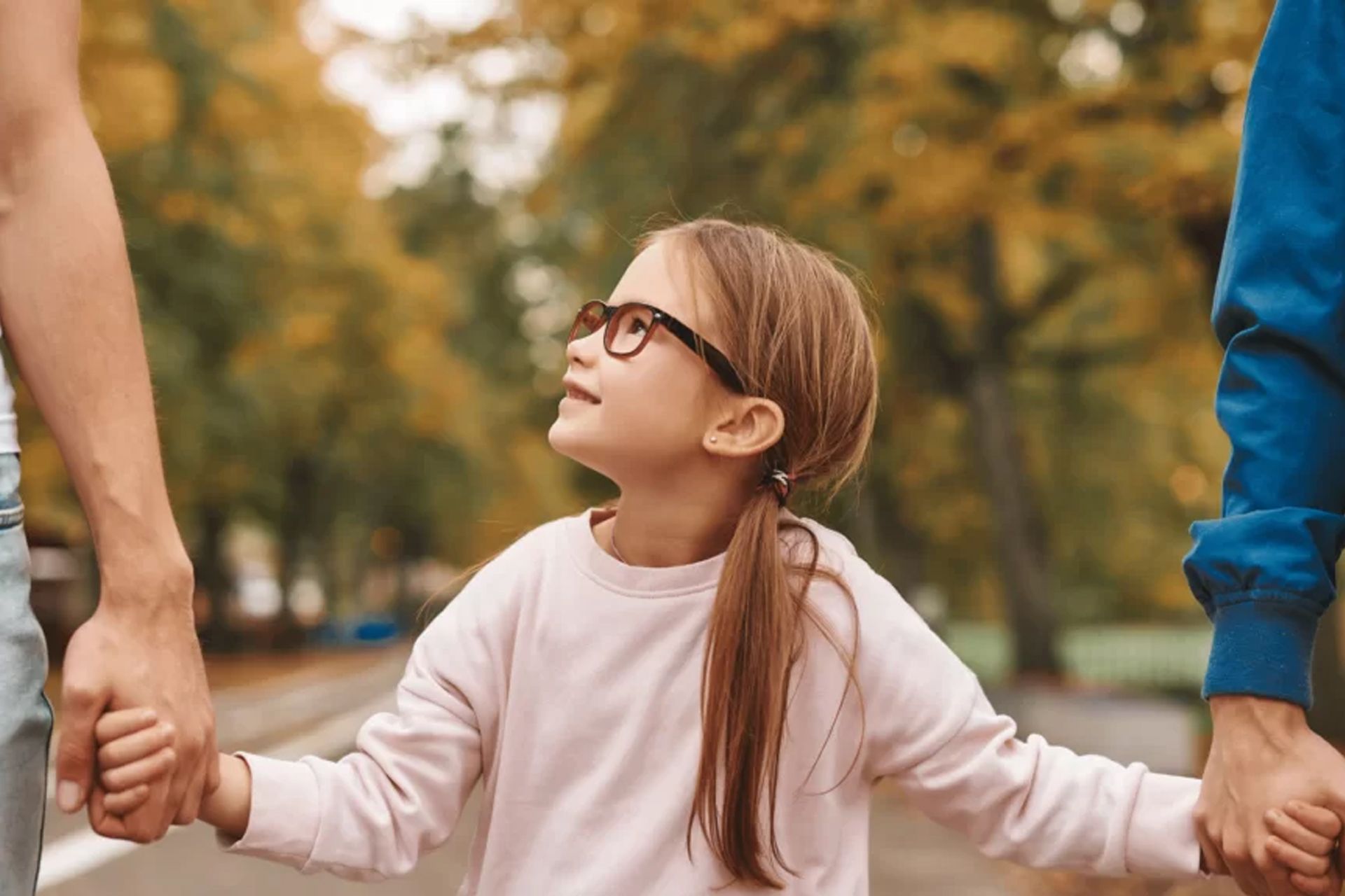 A little girl is holding hands with her parents in a park.
