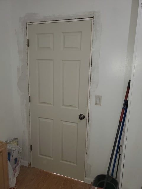 A white door is sitting in a room next to a broom.