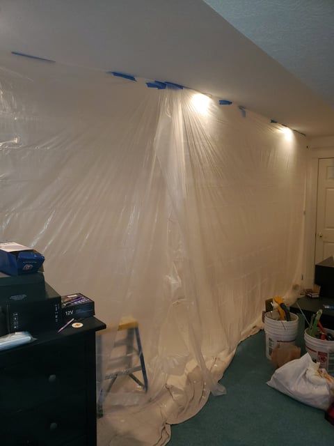A room with a wall covered in plastic and a ladder.