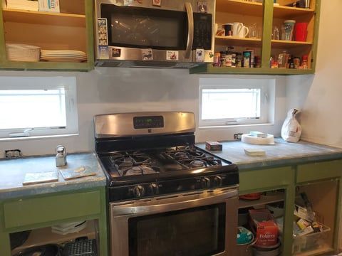A kitchen with a stove , microwave , and green cabinets.