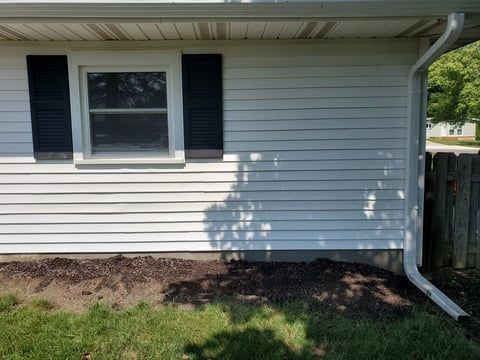 A white house with black shutters and a gutter on the side of it.