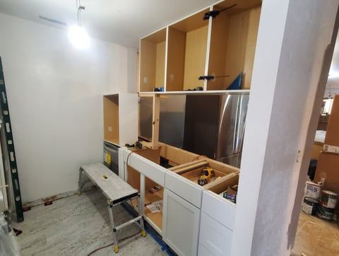 A kitchen is being remodeled with white cabinets and stainless steel appliances.