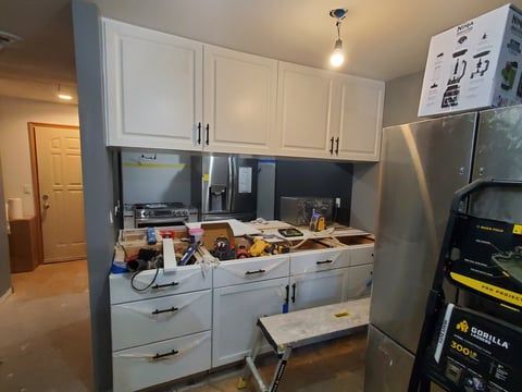 A kitchen is being remodeled with white cabinets and stainless steel appliances.