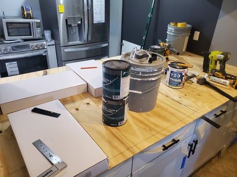 A kitchen counter with buckets of paint and tools on it.