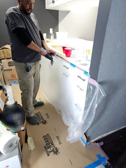 A man is standing in a kitchen with a cardboard box that says ' timber ' on it
