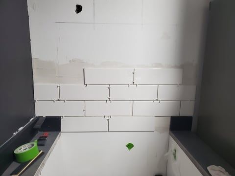 A bathroom with white tiles being installed on the wall.