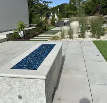 Concrete bench with blue mosaic top beside a tiled patio, lawn, and landscaped garden with steps and fountain grass