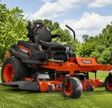 Orange-and-black riding lawn mower on green grass in a sunny yard