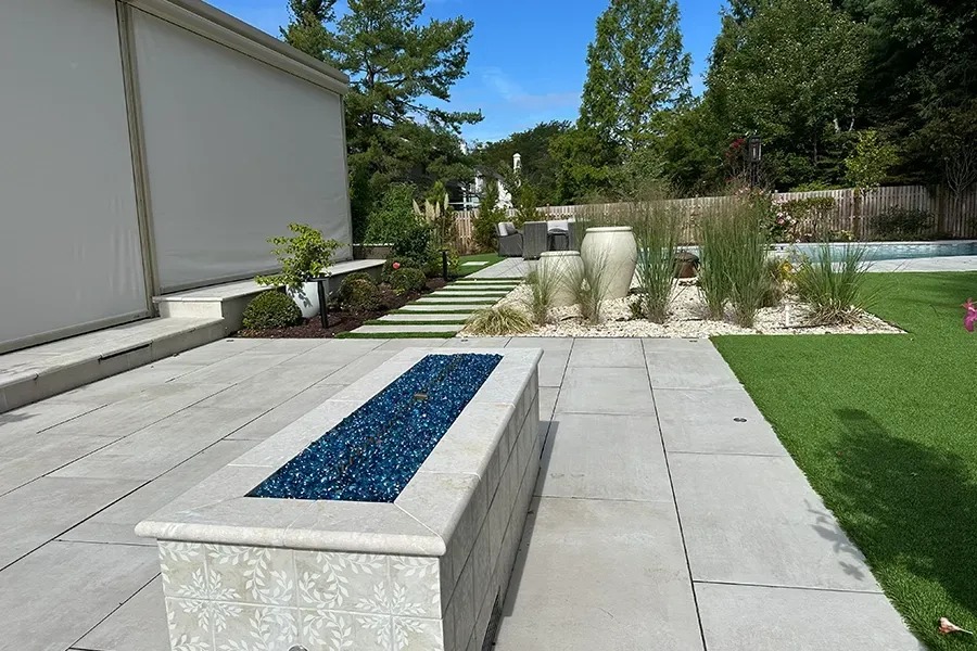 Modern backyard patio with stone benches, steps, grass, and a water feature.