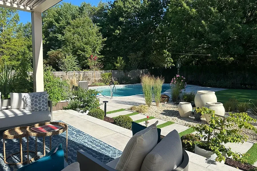 Backyard patio with pool, lounge chairs, and lush green landscaping in bright sunlight