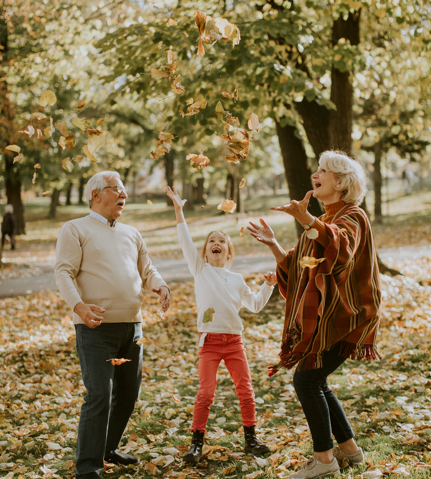 Grandparents and child tossing autumn leaves in a park; joyful expressions, fall foliage.