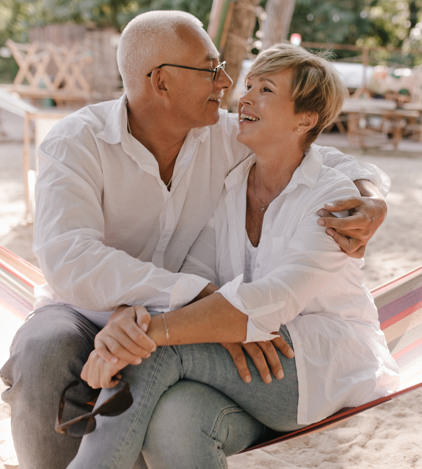 Elderly couple in a hammock, smiling and embracing outdoors.