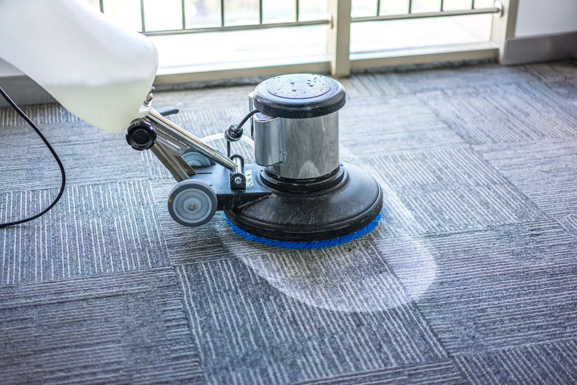 Floor buffer cleaning gray carpet near a sunlit window